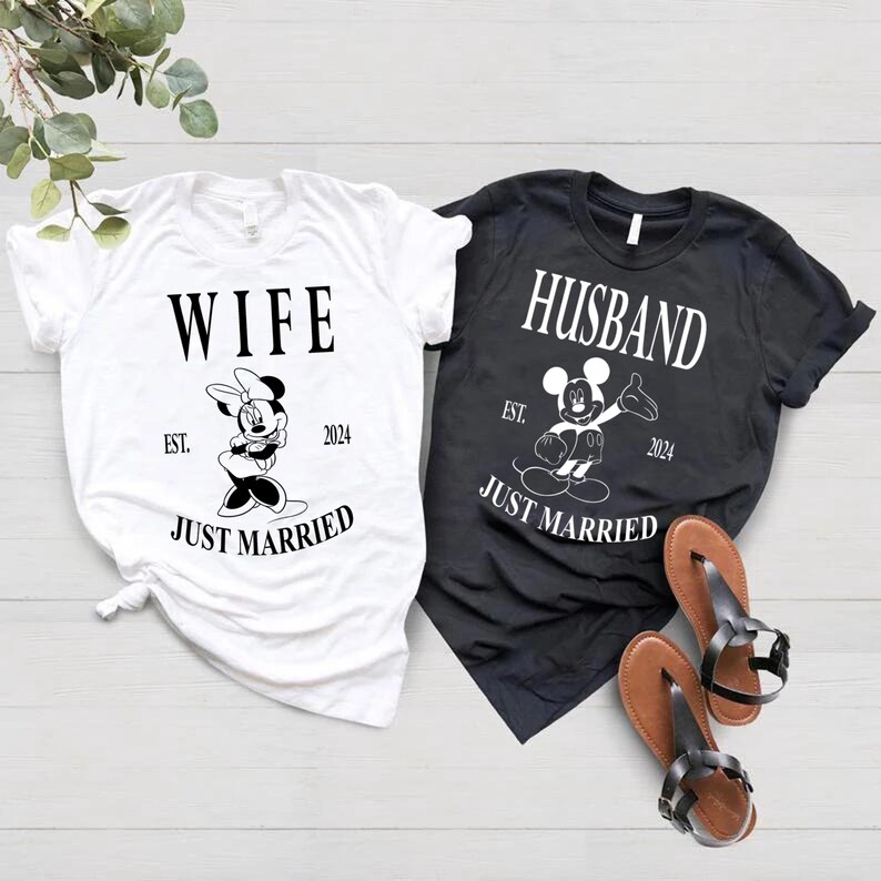 May include: A white t-shirt with the word "WIFE" and a black and white image of Minnie Mouse. The shirt also says "EST. 2024" and "JUST MARRIED". A black t-shirt with the word "HUSBAND" and a black and white image of Mickey Mouse. The shirt also says "EST. 2024" and "JUST MARRIED".