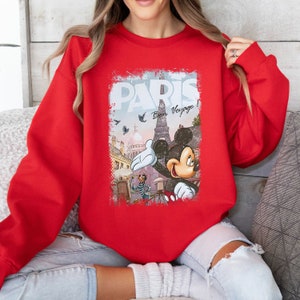 May include: Red sweatshirt with a graphic print of Mickey Mouse in front of the Eiffel Tower in Paris. The graphic also includes the text "Paris" and "Bon Voyage!"