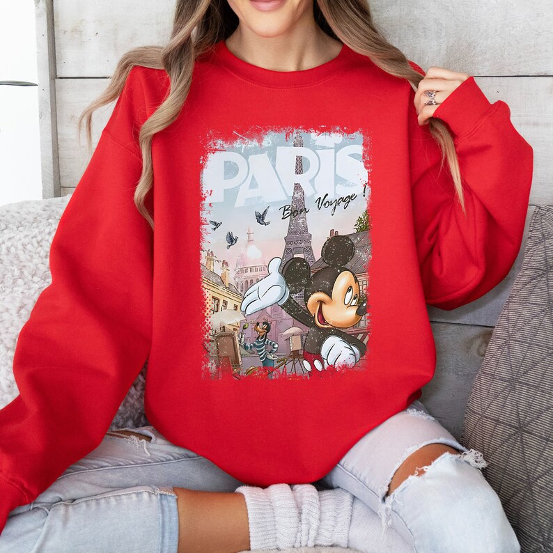May include: Red sweatshirt with a graphic print of Mickey Mouse in front of the Eiffel Tower in Paris. The graphic also includes the text "Paris" and "Bon Voyage!"
