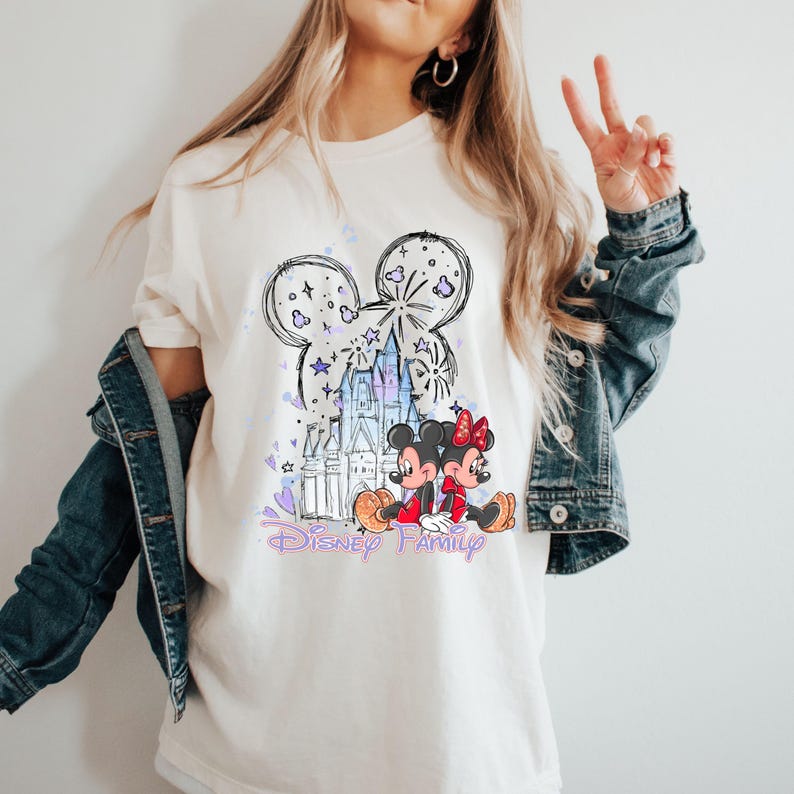 May include: Cream-coloured t-shirt with a Disney design. The graphic features a Mickey Mouse head outline, a castle, and Mickey and Minnie Mouse characters. The words "Disney Family" are written in a purple script.