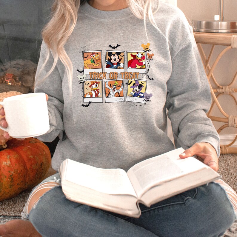 Op de afbeelding: Een grijs sweatshirt met een grafische print van verschillende Disney-personages gekleed in Halloween-kostuums. De print bevat de tekst "Trick or Treat".