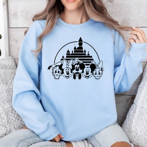 May include: A light blue sweatshirt with a black graphic of Mickey Mouse, Minnie Mouse, Donald Duck, and Goofy in front of the iconic Cinderella's Castle at Walt Disney World.