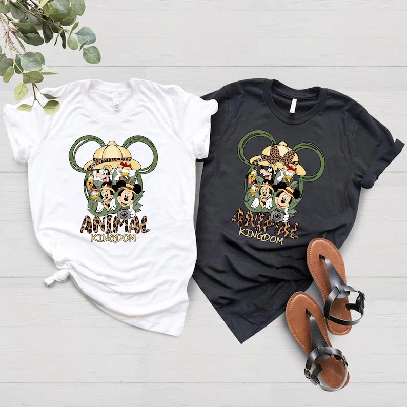 May include: Two t-shirts with a Mickey Mouse head design featuring various Disney characters inside the ears. The text "Animal Kingdom" is printed below the design. One shirt is white and the other is black.