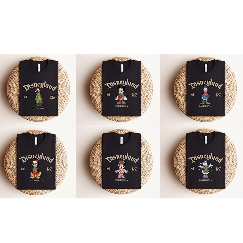 May include: Six black t-shirts with the Disneyland logo and the year 1955. Each shirt features a different Disney character: a Christmas tree, Mickey Mouse, Donald Duck, Goofy, Minnie Mouse, and Daisy Duck. The shirts are displayed on round, woven mats.