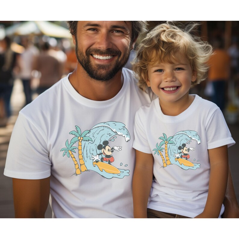 May include: White t-shirts featuring a graphic of Mickey Mouse surfing on a wave with palm trees. The shirts are for adults and children.