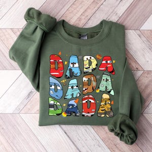 May include: Green sweatshirt with a graphic of the Cars characters spelling out "DADA" in colorful letters.