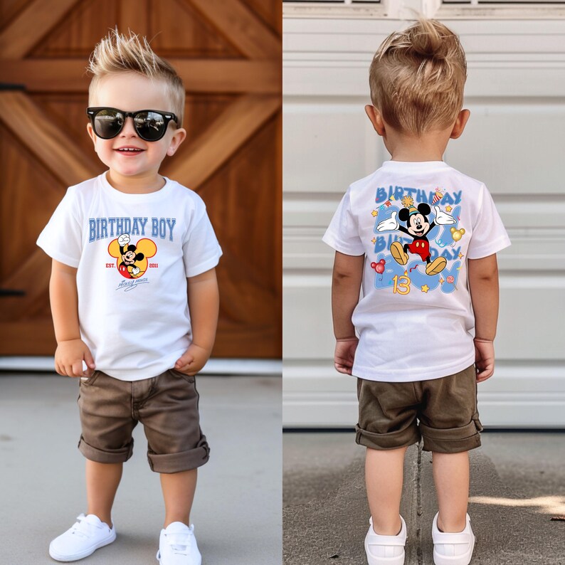 May include: A young boy wearing a white t-shirt with a Mickey Mouse graphic and the text "Birthday Boy" on the front. The back of the shirt has a larger Mickey Mouse graphic with the text "Birthday Boy" and the number "13". The boy is also wearing brown shorts and white trainers.
