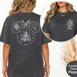 May include: Dark grey t-shirt with a white graphic on the back featuring a castle, fireworks, and the text "The Happiest Place on Earth." A smaller graphic on the front says "Mommy." The shirt is part of the Comfort Colors Pepper collection.