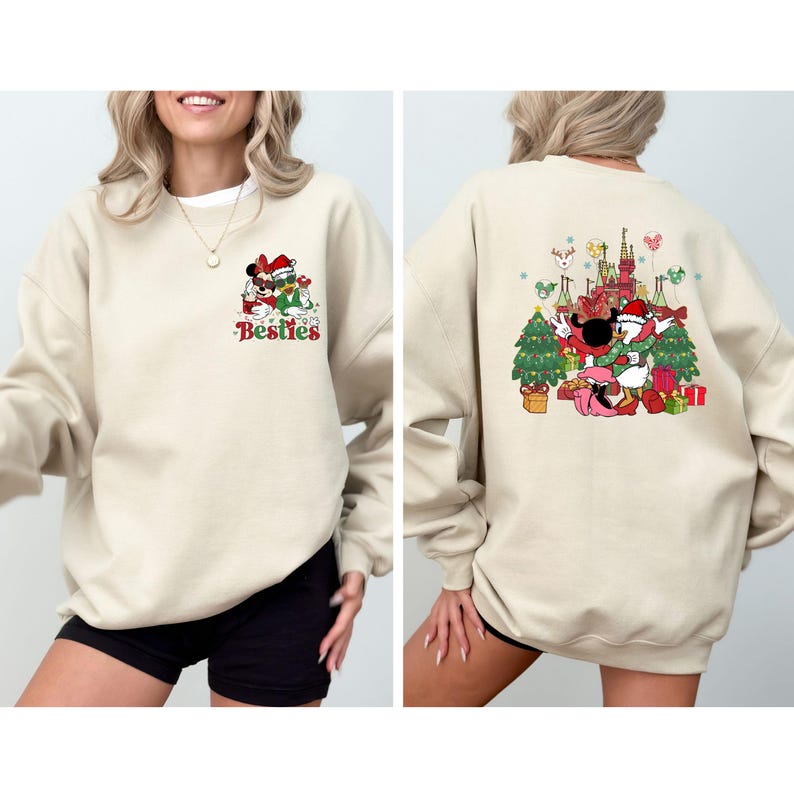 May include: Beige sweatshirt featuring a Christmas-themed graphic of Mickey and Minnie Mouse. The front displays the word "Besties" with the characters wearing Santa hats. The back shows the characters with a Christmas tree and castle.