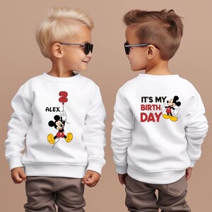 Puede incluir: Dos sudaderas blancas con un dise&ntilde;o de Mickey Mouse. Una sudadera dice "Es mi cumplea&ntilde;os" y la otra dice "Alex" con un globo n&uacute;mero 2.