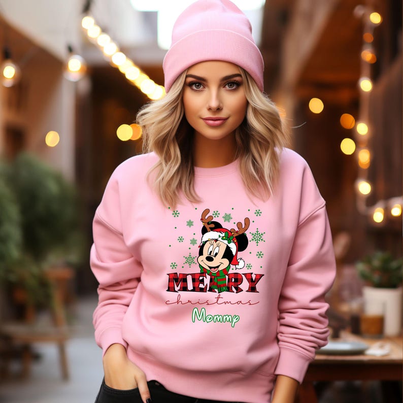 May include: Pink Christmas sweatshirt with a Mickey Mouse design wearing a Santa hat and reindeer antlers. The text on the sweatshirt says "Merry Christmas Mommy".