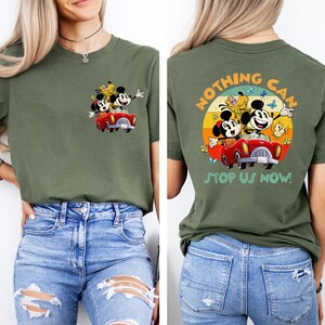 May include: A green t-shirt with a vintage-style graphic of Mickey Mouse, Minnie Mouse, and Pluto driving a red car. The text "Nothing Can Stop Us Now!" is printed on the back of the shirt.