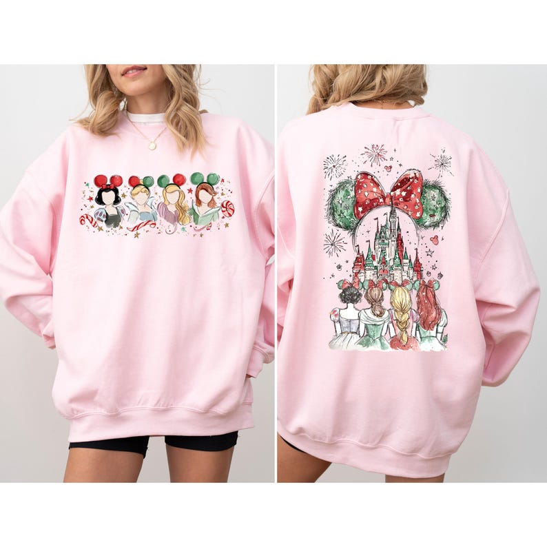 May include: A light pink sweatshirt featuring a watercolor design of Disney princesses. The front shows the princesses with Mickey Mouse ears. The back displays a castle with Mickey Mouse ears and a red bow.