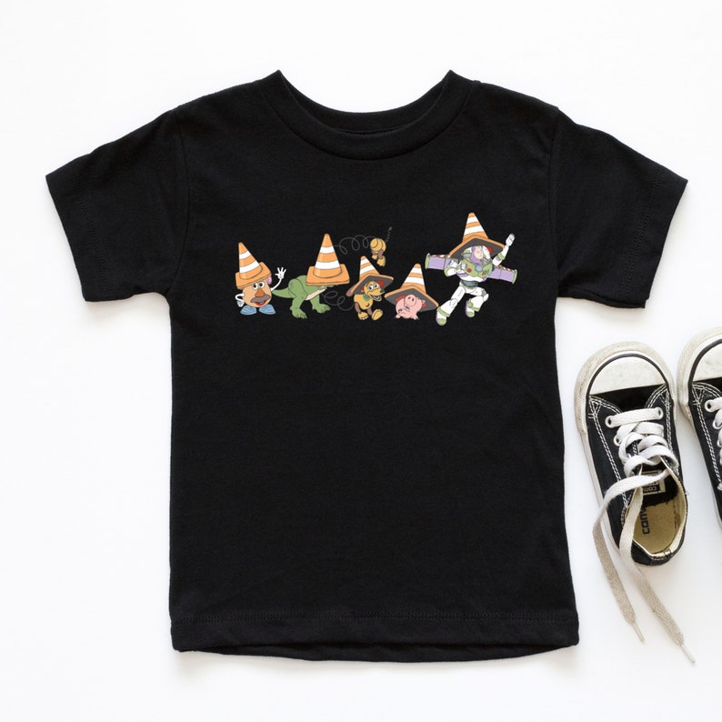 Op de afbeelding: Zwart T-shirt met een afbeelding van Toy Story-personages die verkeerskegels dragen. De personages zijn Woody, Buzz Lightyear, Rex, Mr. Potato Head en Hamm.
