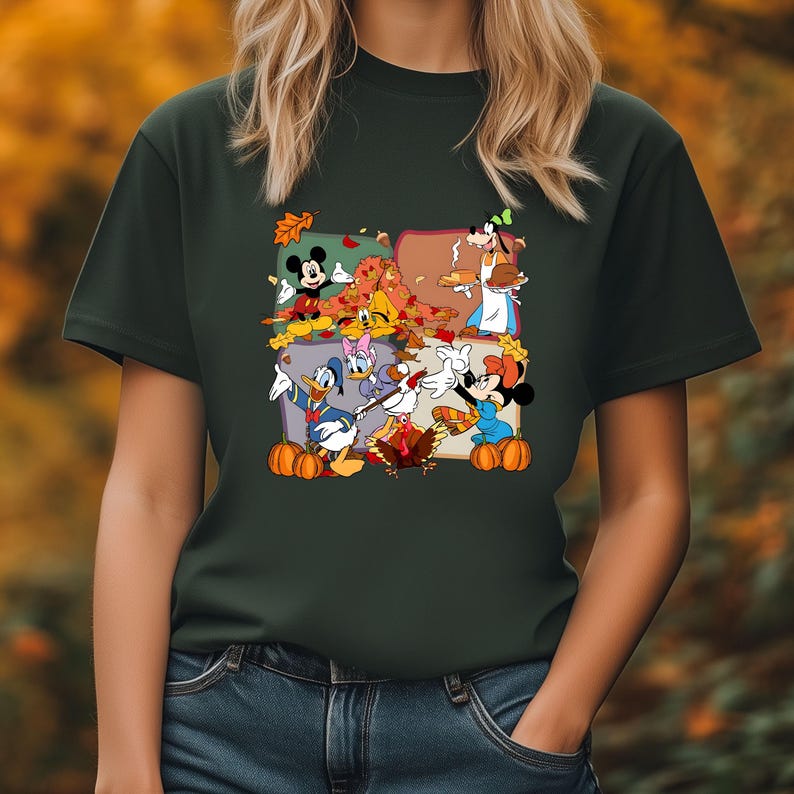 May include: Dark green t-shirt featuring a colorful graphic of Disney characters celebrating Thanksgiving. Mickey Mouse, Minnie Mouse, Donald Duck, and Goofy are depicted with pumpkins and autumn leaves. The shirt is made of a soft material.