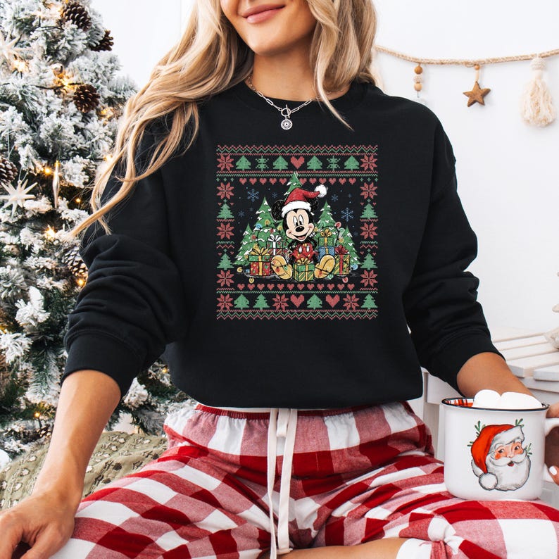 May include: Black sweatshirt featuring a festive Christmas design with Mickey Mouse wearing a Santa hat, surrounded by Christmas trees and gifts. The design incorporates red, green, and white elements, creating a holiday theme. The sweatshirt is paired with red and white plaid pajama pants.
