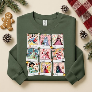 Puede incluir: Sudadera verde oscuro con nueve im&aacute;genes enmarcadas de princesas de Disney en entornos navide&ntilde;os festivos. Cada imagen es una foto estilo polaroid. Las princesas incluyen Blancanieves, Cenicienta, Bella, Tiana, Priscilla y otras.