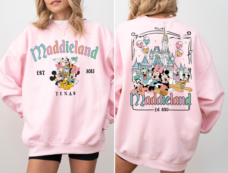 May include: Pink sweatshirt with a graphic of Mickey Mouse and friends in front of a castle. The text "Maddieland Est. 2023 Texas" is printed on the front of the sweatshirt. The back of the sweatshirt has a graphic of Mickey Mouse and friends in front of a castle with the text "Maddieland Est. 2023".