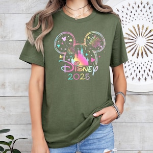 May include: A green t-shirt with a rainbow-colored Mickey Mouse head silhouette featuring a castle and fireworks. The text "DISNEY 2025" is printed below the silhouette.