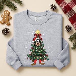 May include: A light gray sweatshirt featuring a Christmas tree design with Goofy's face. The tree is decorated with ornaments, lights, and a star. The sweatshirt has a crew neck and long sleeves.
