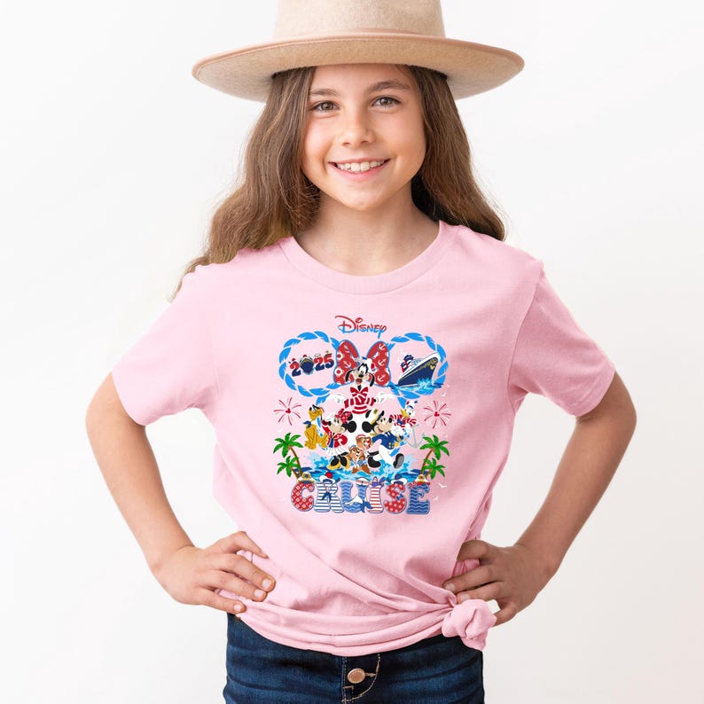 May include: A light pink t-shirt featuring a Disney Cruise design. The graphic includes Mickey and Minnie Mouse, a cruise ship, and the text "2025 Cruise". The design is in shades of red, blue, and white.