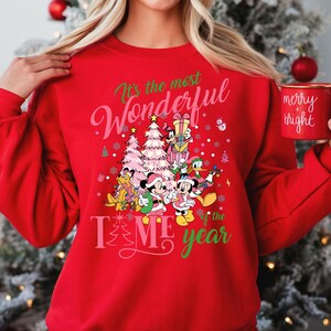 May include: Red Christmas sweatshirt with a festive design featuring Mickey Mouse and friends. The text reads "It's the most Wonderful Time of the Year".