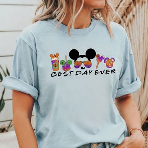 May include: Light blue t-shirt with a black graphic of Mickey Mouse and other Disney characters wearing Halloween costumes. The text "BEST DAY EVER" is printed below the graphic.