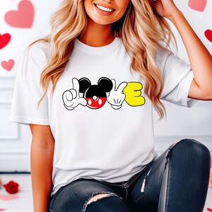 May include: White t-shirt with a graphic of Mickey Mouse's hands forming the word "LOVE" with Mickey Mouse's head in the middle.