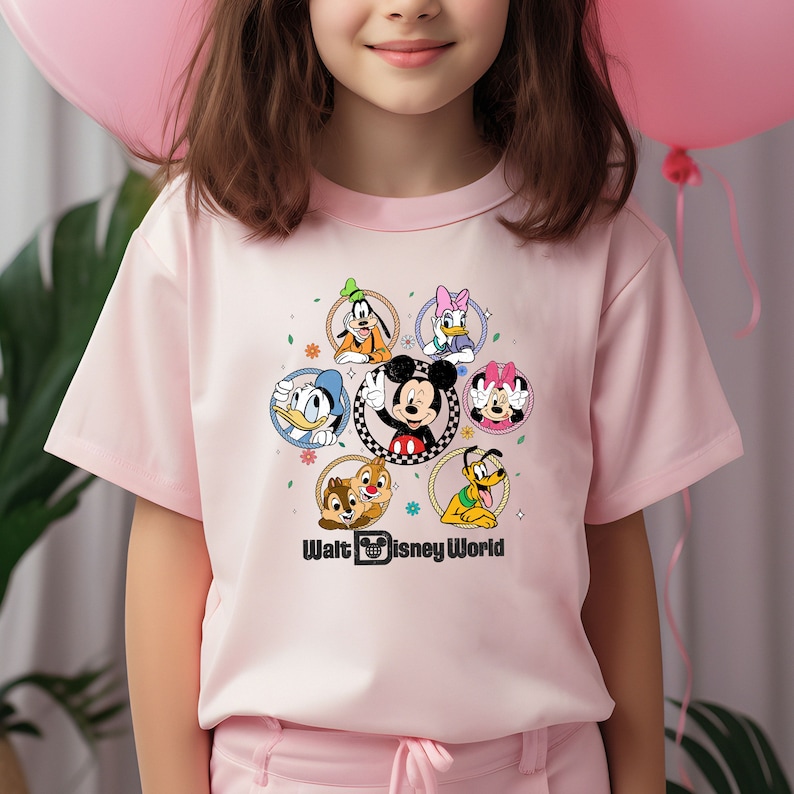 May include: Pink short-sleeved t-shirt with a colorful graphic of Mickey Mouse and other Disney characters in a circle. The text "Walt Disney World" is printed below the graphic.