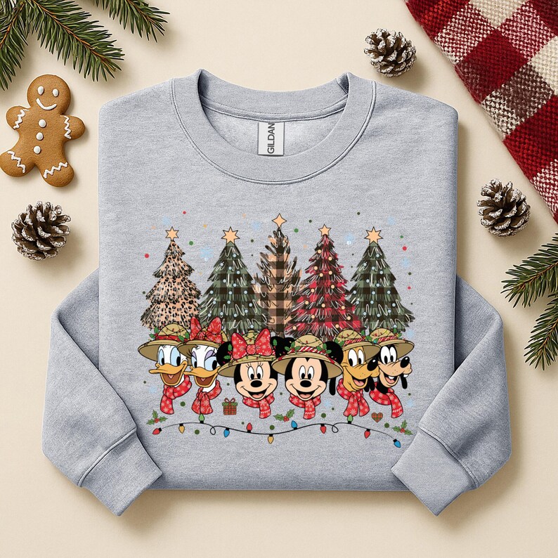 May include: A light gray sweatshirt featuring a festive design with Disney characters and Christmas trees. The characters are wearing hats and scarves, with a string of lights at the bottom. The trees have various patterns.