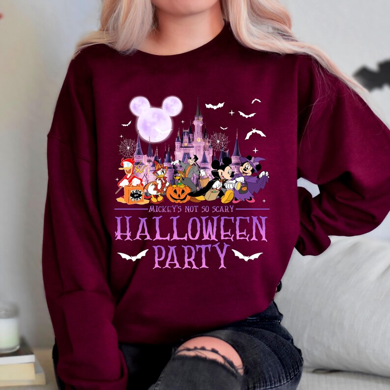 Puede incluir: Una sudadera color burdeos con un gr&aacute;fico morado de Mickey Mouse y sus amigos frente al castillo de Disney. El texto "Mickey's not so scary Halloween Party" est&aacute; impreso en la sudadera.