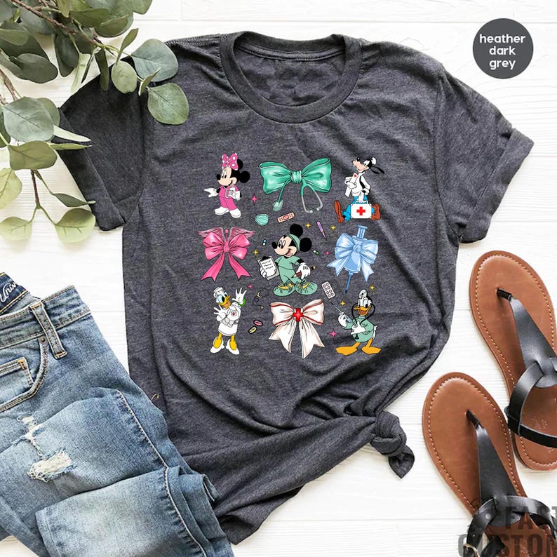 Pu&ograve; includere: T-shirt grigio scuro con personaggi dei cartoni animati e fiocchi. Il design include Minnie Mouse, Mickey Mouse, Paperino e Pippo, insieme a fiocchi ed elementi a tema medico. La maglietta &egrave; abbinata a jeans blu e sandali.