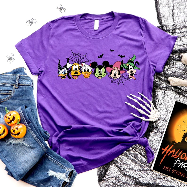 Pu&ograve; includere: Maglietta viola con una grafica di Topolino, Minnie Mouse, Paperino, Pippo e Pluto vestiti con costumi di Halloween. I personaggi sono davanti a una ragnatela e pipistrelli.