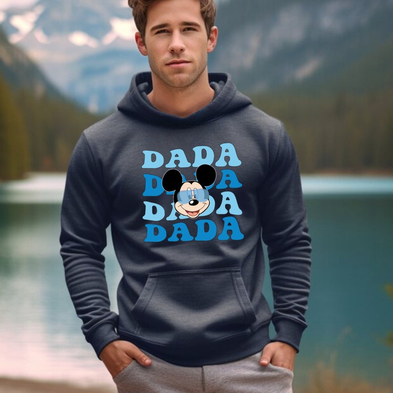 May include: A dark blue hooded sweatshirt with a graphic of Mickey Mouse wearing sunglasses and the word "DADA" repeated in a blue gradient.