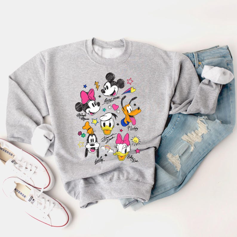 May include: A gray sweatshirt with a colorful cartoon print of Mickey Mouse, Minnie Mouse, Donald Duck, Goofy, and Pluto. The characters are drawn in a doodle style with stars, hearts, and lightning bolts.