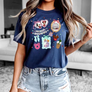 May include: A navy blue t-shirt with a graphic print of various Disney characters and icons, including Mickey Mouse, Minnie Mouse, a dragon, a donut, and a coffee cup. The text "EPCOT CENTER" is printed on the shirt.