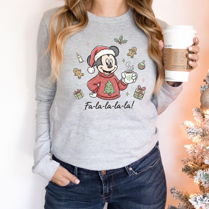 May include: A gray long-sleeve shirt featuring a Christmas-themed Mickey Mouse graphic. Mickey is wearing a Santa hat and a red sweater with a Christmas tree. The shirt has the text "Fa-la-la-la-la!" below the graphic.