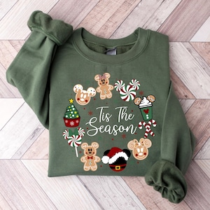 Peut inclure: Un sweat-shirt vert avec un motif de No&euml;l. Le motif comprend des t&ecirc;tes de Mickey Mouse en pain d'&eacute;pices, des cannes en sucre, un sapin de No&euml;l et le texte "Tis The Season". Le sweat-shirt a des manches longues.