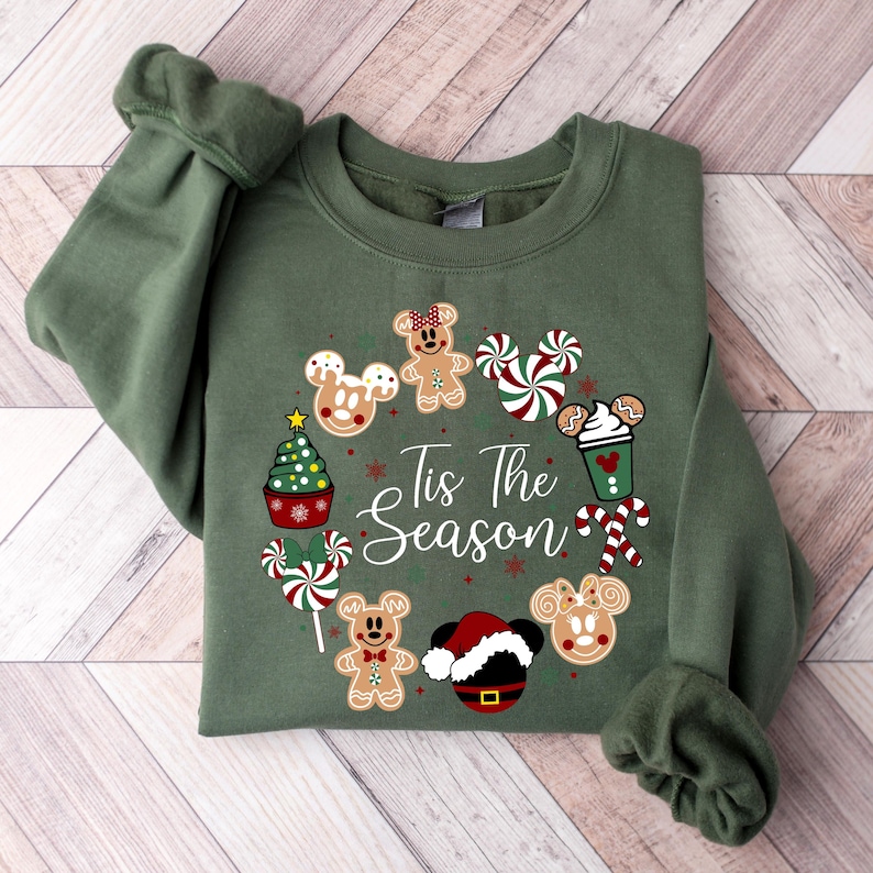 Peut inclure: Un sweat-shirt vert avec un motif de No&euml;l. Le motif comprend des t&ecirc;tes de Mickey Mouse en pain d'&eacute;pices, des cannes en sucre, un sapin de No&euml;l et le texte "Tis The Season". Le sweat-shirt a des manches longues.