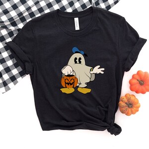 Puede incluir: Camiseta negra con un fantasma de dibujos animados que lleva un sombrero azul y sostiene una calabaza de Halloween. El fantasma est&aacute; vestido como Mickey Mouse.
