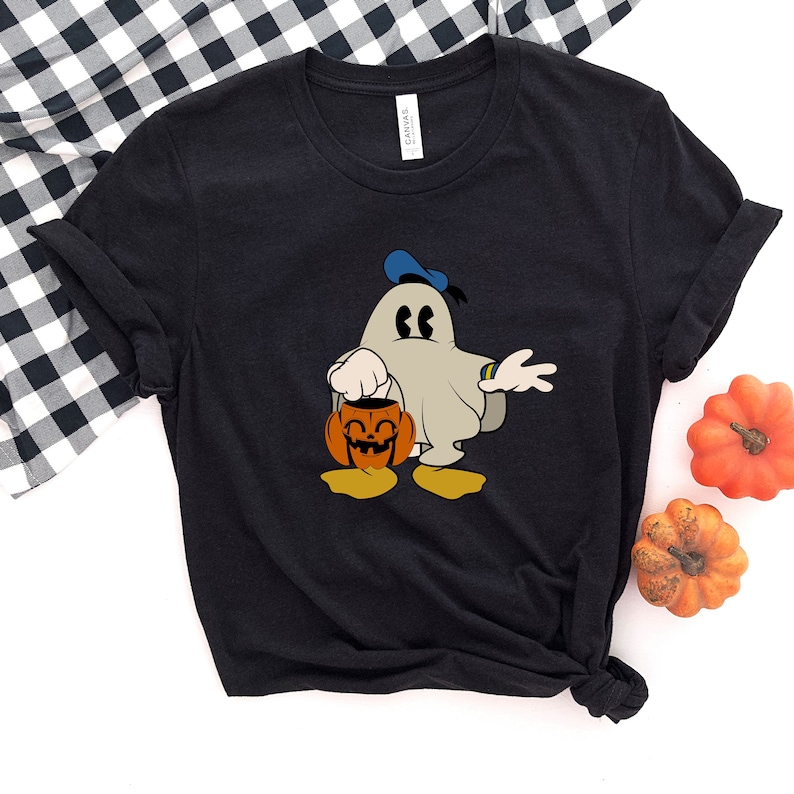 Puede incluir: Camiseta negra con un fantasma de dibujos animados que lleva un sombrero azul y sostiene una calabaza de Halloween. El fantasma est&aacute; vestido como Mickey Mouse.