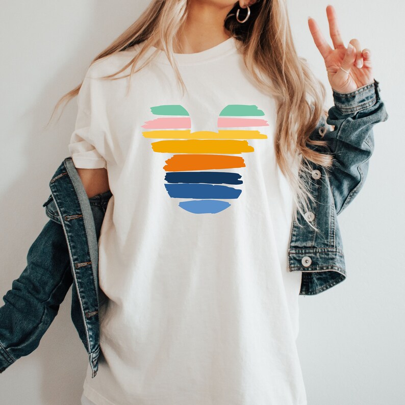 May include: A white t-shirt with a colorful Mickey Mouse silhouette design. The silhouette is made up of horizontal stripes in shades of pink, green, yellow, orange, blue, and white.