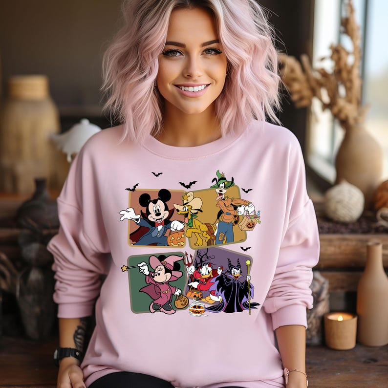 K&ouml;nnte beinhalten: Rosafarbener Pullover mit einem Grafikdruck von Mickey Mouse, Pluto, Goofy, Donald Duck und Maleficent in Halloween-Kost&uuml;men. Die Figuren halten K&uuml;rbisse und S&uuml;&szlig;igkeiten.