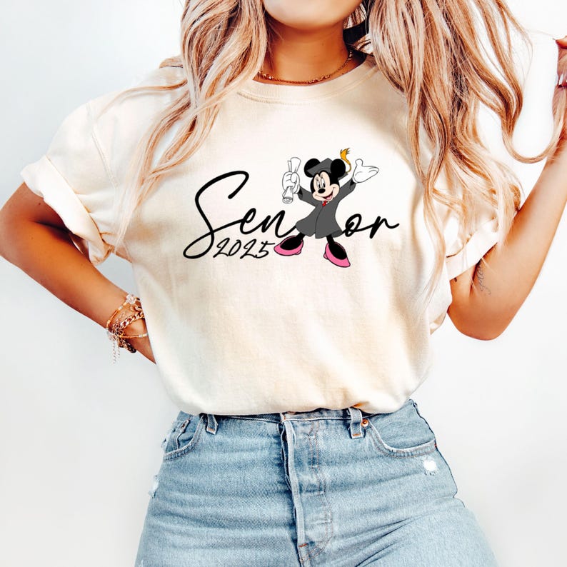 May include: White t-shirt featuring a black and white illustration of Mickey Mouse wearing a graduation cap and gown. The text "Senior 2023" is written in black cursive.