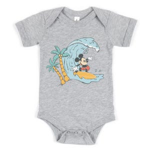 May include: A grey short-sleeved baby bodysuit with a graphic of Mickey Mouse surfing on a wave with palm trees in the background.