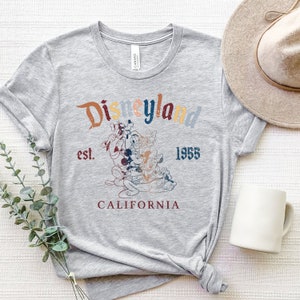 May include: Gray t-shirt with a vintage-style graphic of Mickey Mouse and friends in front of the Disneyland logo. The text reads "Disneyland est. 1955 California".
