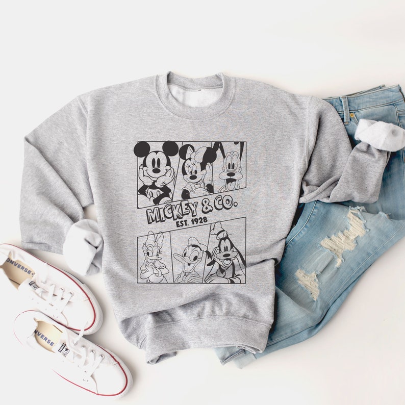 K&ouml;nnte beinhalten: Ein graues Sweatshirt mit einem schwarz-wei&szlig;en Grafikdruck von Mickey Mouse, Minnie Mouse, Donald Duck und Goofy. Die Grafik enth&auml;lt den Text "Mickey & Co. Est. 1928".