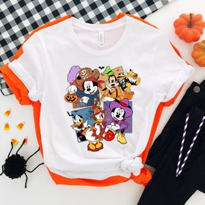 May include: White t-shirt with a colorful graphic print of Mickey Mouse, Minnie Mouse, Donald Duck, Goofy, and Pluto dressed in Halloween costumes. The characters are holding candy and pumpkins.