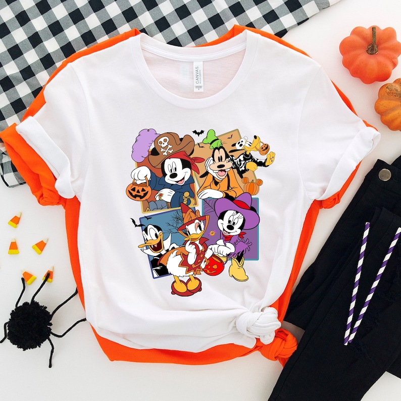 May include: White t-shirt with a colorful graphic print of Mickey Mouse, Minnie Mouse, Donald Duck, Goofy, and Pluto dressed in Halloween costumes. The characters are holding candy and pumpkins.