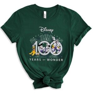 May include: A green t-shirt with a graphic of Mickey Mouse, Minnie Mouse, Donald Duck, Goofy, and Pluto celebrating Disney's 100th anniversary. The graphic includes the text "Disney" and "100 Years of Wonder".